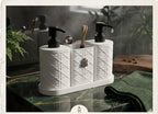 A white bathroom vanity organizer set with two black pump bottles, a toothbrush holder, and a small metal spoon holder, styled on a green marble countertop with a folded green towel and mirror reflections in the background.