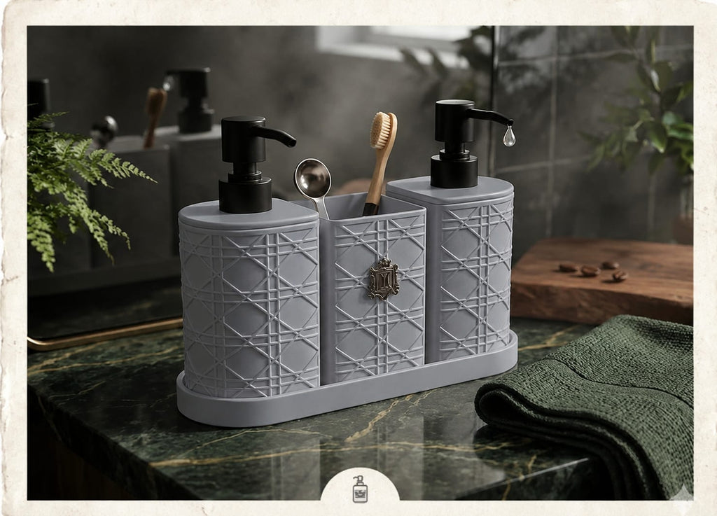 A gray three-compartment bathroom organizer with embossed geometric patterns, black pump dispensers, a wooden toothbrush, and a metal spoon, set on a dark marble countertop in a bathroom.